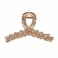 A translucent champagne-colored hair claw clip embellished with clear rhinestones along the curved bar, shown on a plain white background.