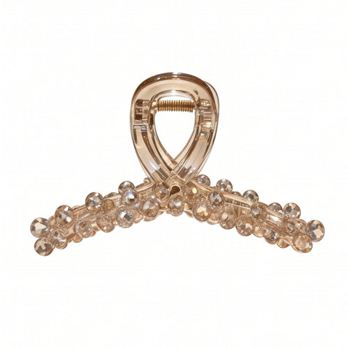 A translucent champagne-colored hair claw clip embellished with clear rhinestones along the curved bar, shown on a plain white background.